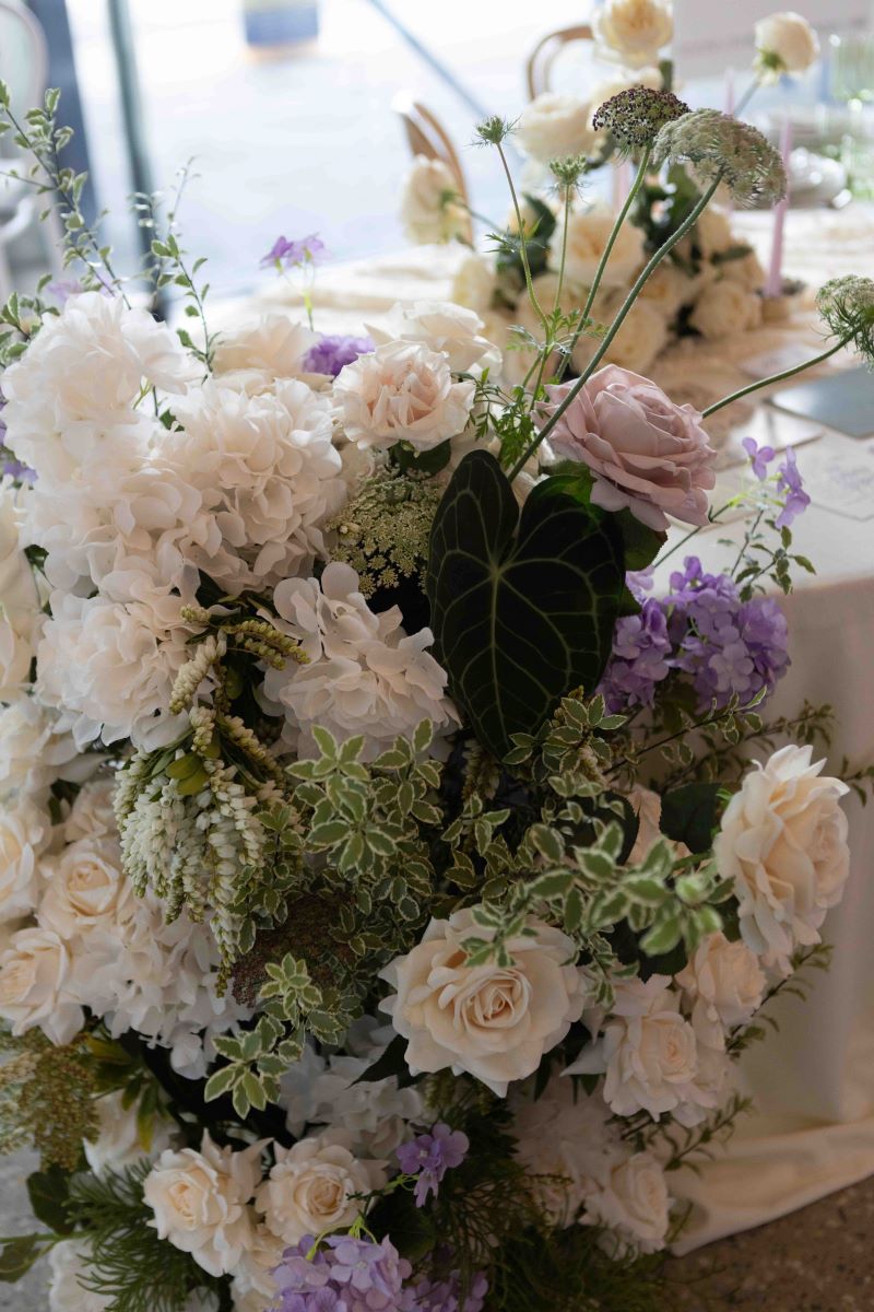 white flowers, pink roses, and a green plant and purpole flowers in a boquet