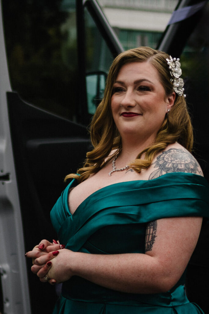 A person in a wedding dress standing in a car doorway smiling