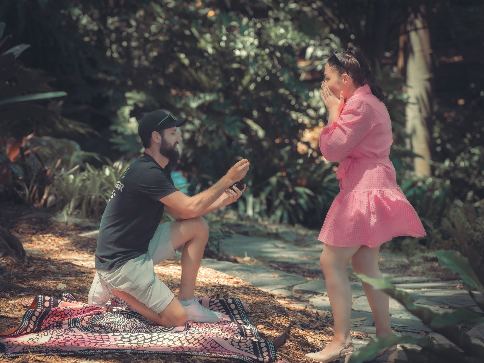 A surprise proposal a woman is covering her mouth in surprise and her partner is down on one knee with a ring 