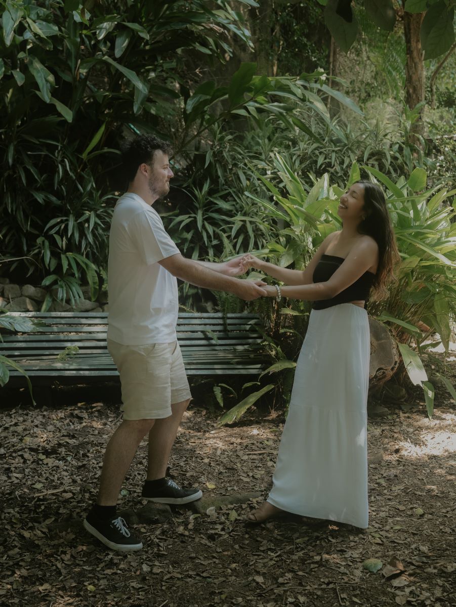 A couple holding hands in a park and laughing together the woman is wearing a black tube top and a white skirt the man is wearing a white shirt and tan pants 
