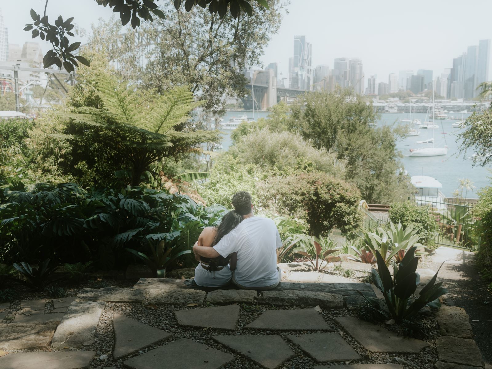 A couple sitting together looking out at the harbour the man has his arm around his partner's shoulder and his partner is leaning into him 