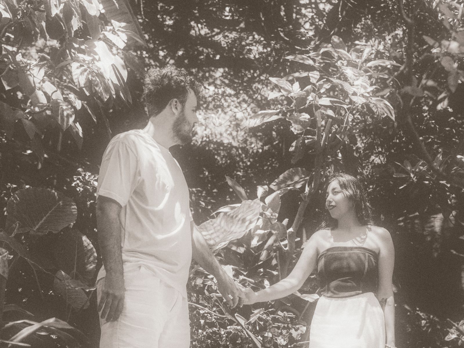 A couple holding hands in a garden together and looking at each other surrounded by different plants 