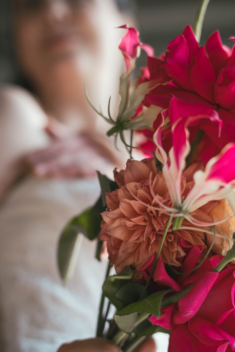 Close-up detail of vibrant red and coral bouquet with bride softly focused in the background—candid wedding photographer capturing intimate moments at Vaucluse estate house